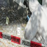 Eine Person in Ganzkörper-Schutzanzug fotografiert einen Bereich. Es sind Schilder mit Nummern aufgestellt. Der Bereich ist durch ein Absperrband mit dem Begriff Polizeiabsperrung abgesperrt. 