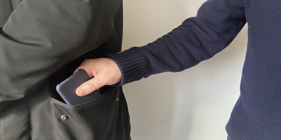 Eine Person nimmt ein Handy aus der Jackentasche einer anderen Person. 