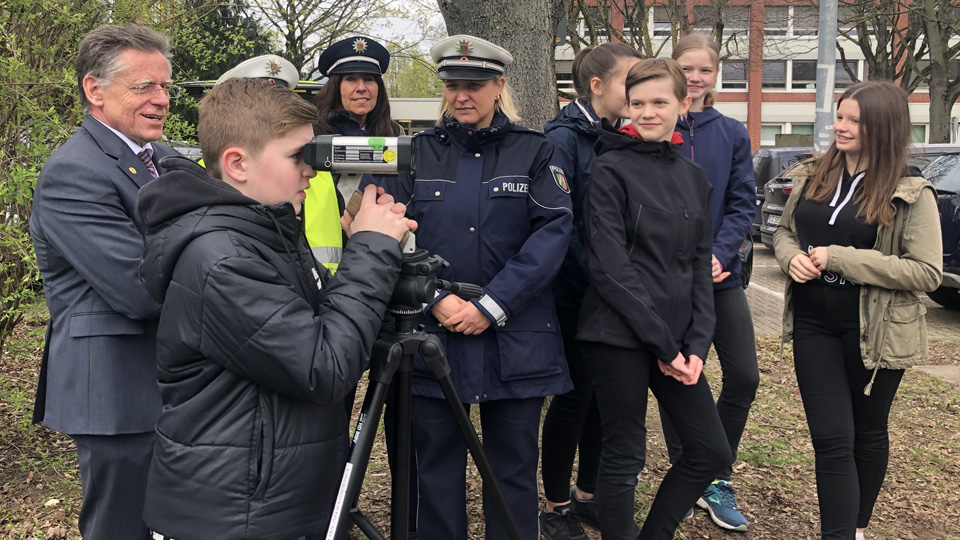 Links ist der Landrat Hans-Jürgen Petrauschke zu sehen. Rechts daneben zwei Polizistinnen. Außerdem weitere Jugendliche und ein Junge schaut durch ein Radarmessgerät. 