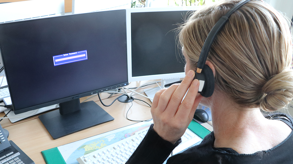 Eine Person mit einem Headset sitzt vor zwei Bildschirmen. 