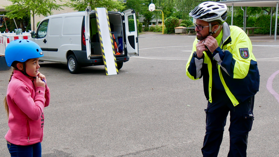 Helme retten Leben! Ein Polizist und ein Mädchen ziehen sich einen Fahrradhelm an. 