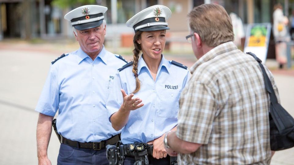 Das Bild zeigt eine Polizeibeamtin und einen Polizeibeamten im Gespräch mit Passanten