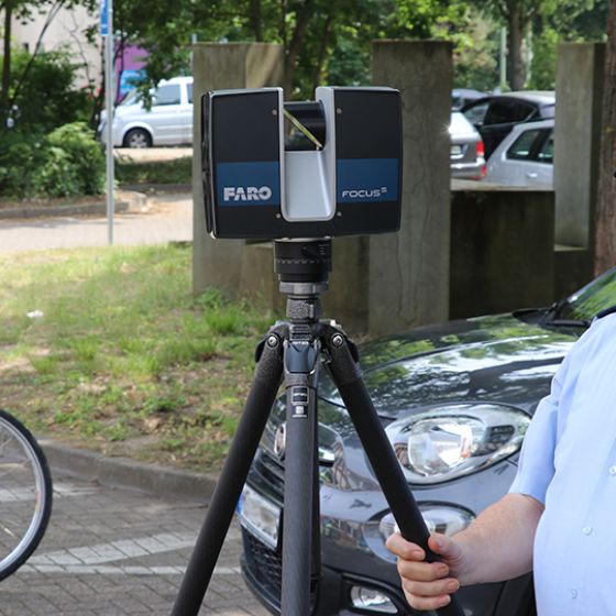 Ein Polizist bedient einen 3D-Scanner. Im Hintergrund liegt ein Fahrrad auf der Straße vor einem Auto.